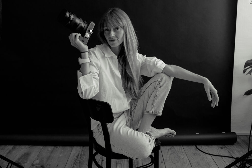 Schwarzweiß-Porträt einer Fotografin im Studio mit Kamera in der Hand.